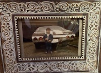 a boy standing next to a car in an ornate frame