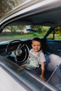 a young boy sitting in the driver's seat of an old car