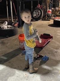 a young boy standing in a garage holding a tool